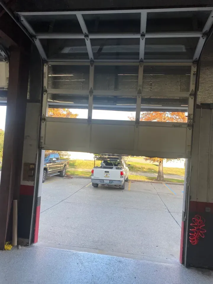 Garage door partially open, revealing a white truck parked outside on a sunny day.
