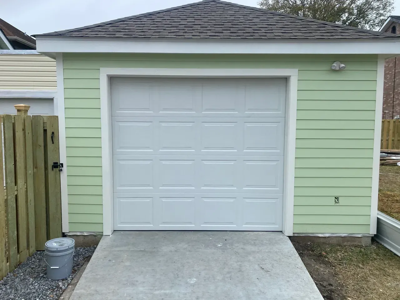 White garage door in a light green building with concrete driveway.