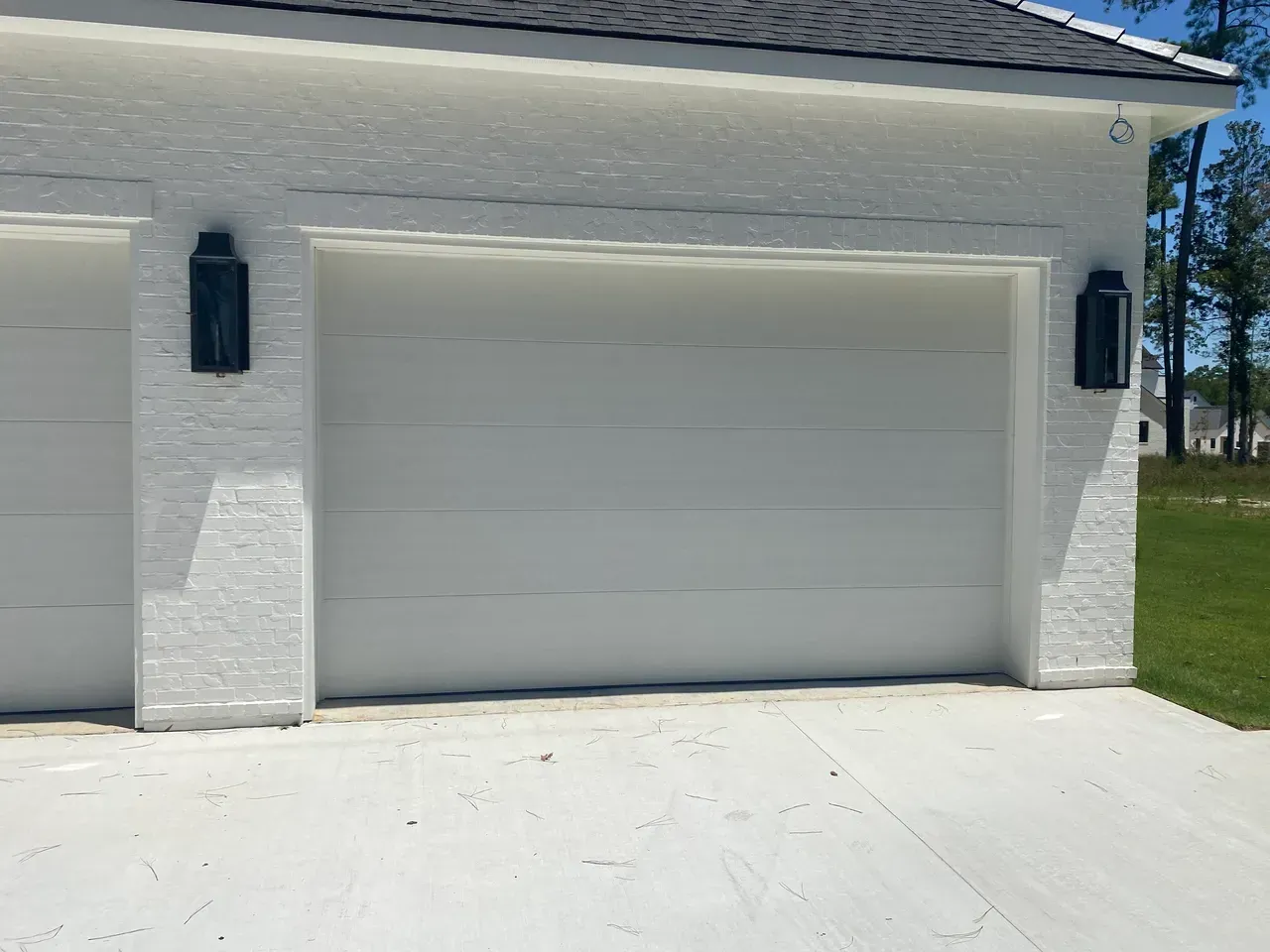 White painted brick garage with a white garage door, black sconces, and concrete driveway.