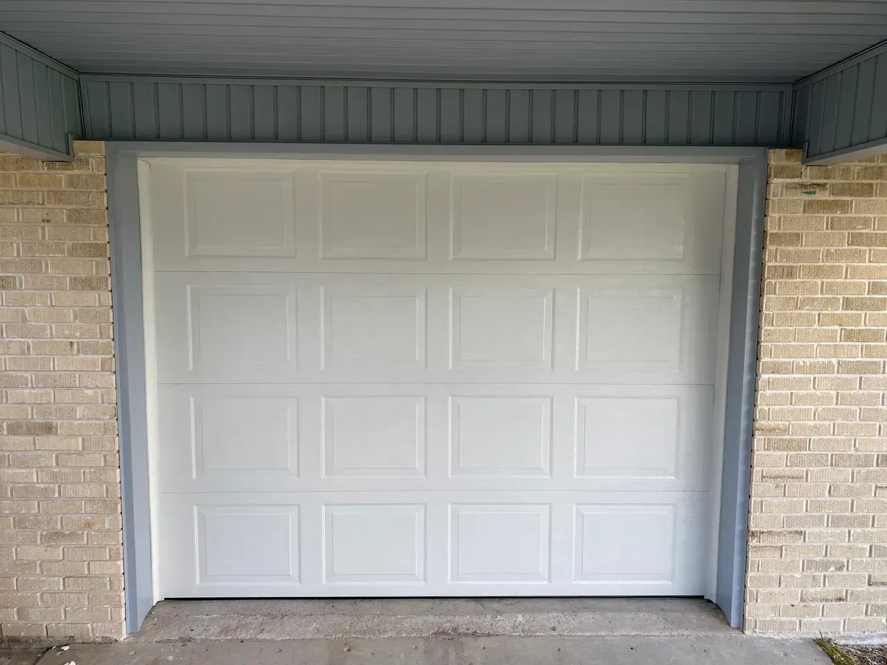 White garage door with gray trim, brick columns, and blue siding above.