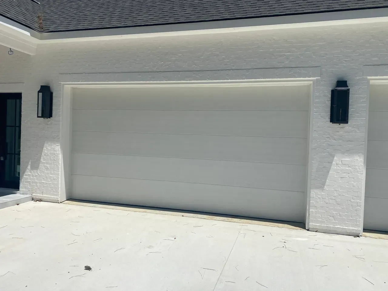 White garage door with two black sconces on a brick exterior.