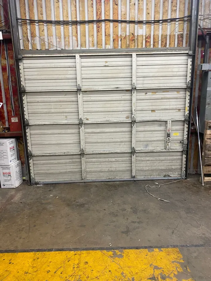 Closed, aged industrial garage door in a warehouse setting, with yellow floor markings.