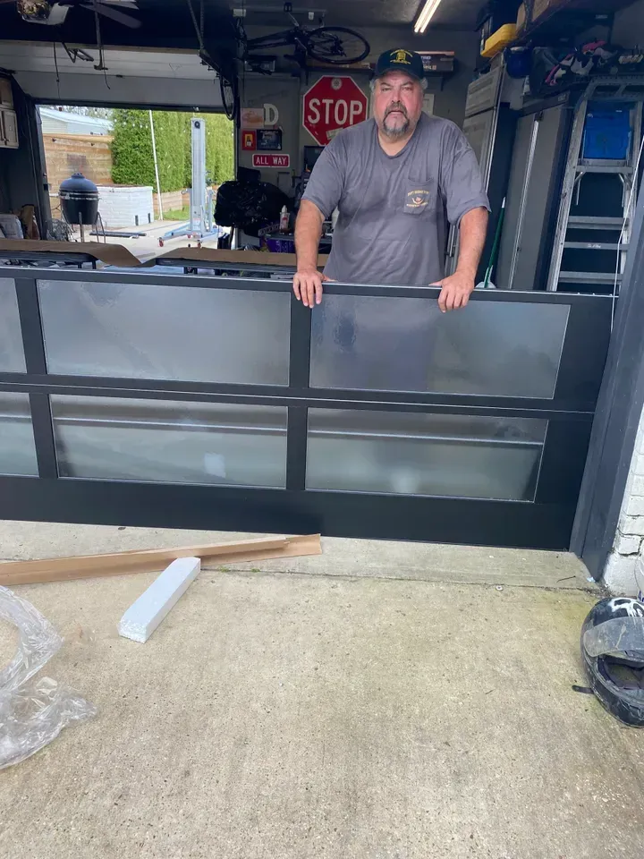 Man in a garage holds a new garage door with frosted glass panels.