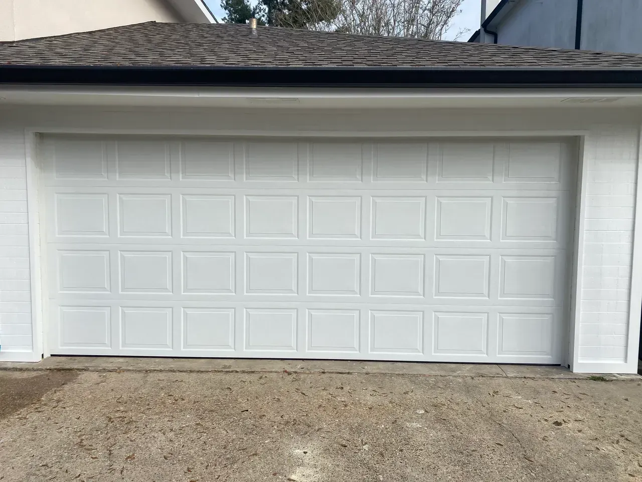 White garage door with grid pattern, in a white frame, against a brown roof and light brown ground.