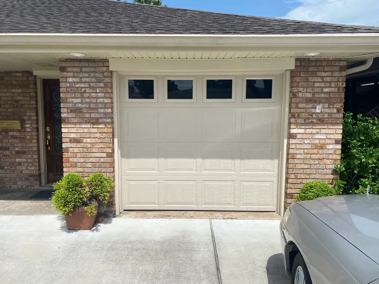 Beige garage door with four small upper windows, flanked by brick columns; a car's front is visible on the right.
