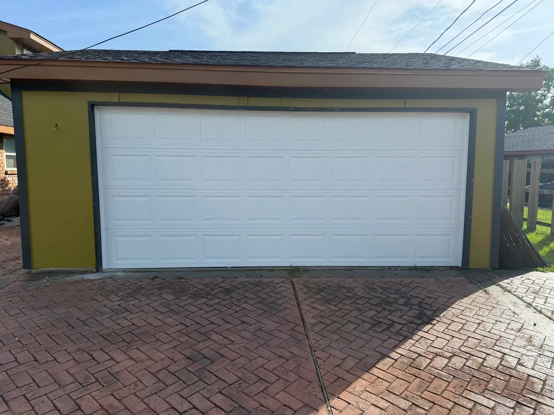 White garage door on a green building with brown trim and a brick driveway.