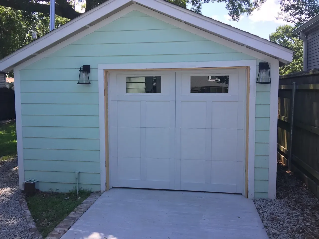 A light green garage with a white door, two windows, and black sconces.