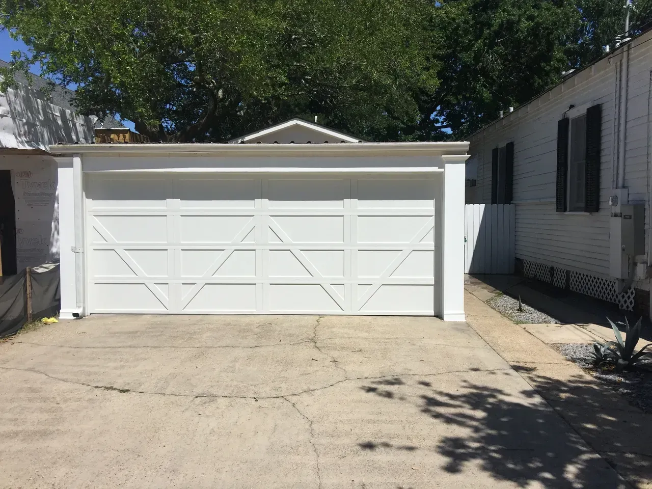 White garage door with diagonal design, next to a white house, on a concrete driveway.