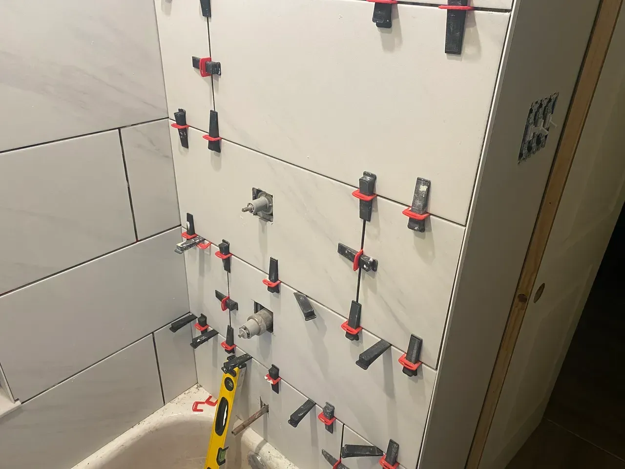 White tiles installed on a bathroom wall, with leveling clips in place. A bathtub is visible below.