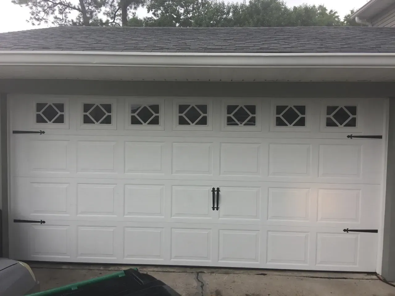 White garage door with diamond-pattern windows, black hardware, and dark roof.