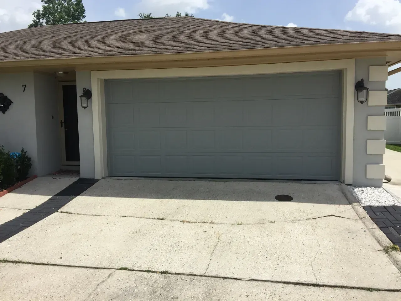 Gray garage door on a light-colored house with a cracked driveway.