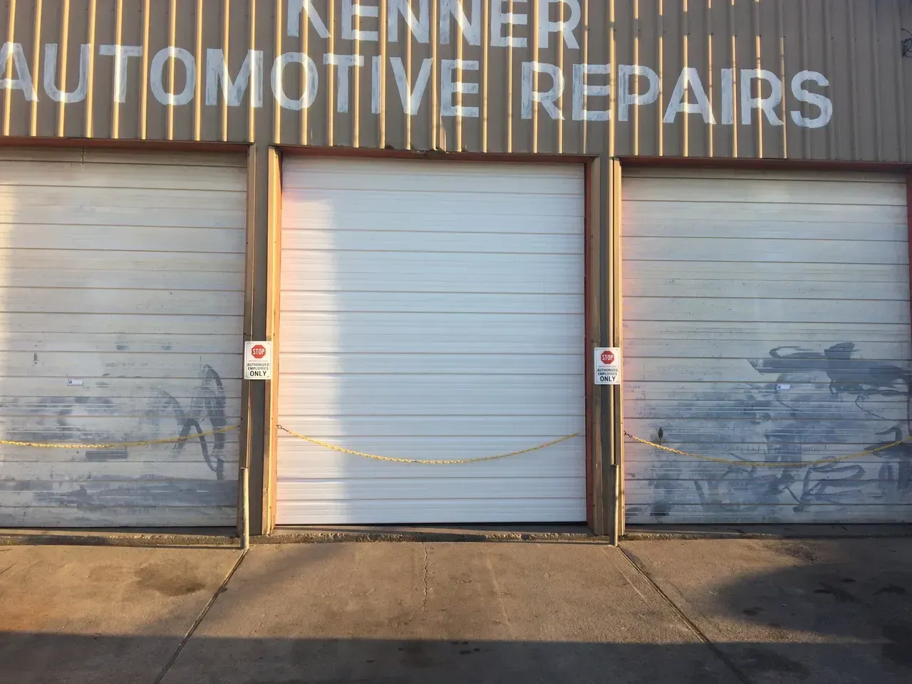 Kenner Automotive Repairs storefront with three closed garage doors. Yellow caution tape and no parking signs are visible.