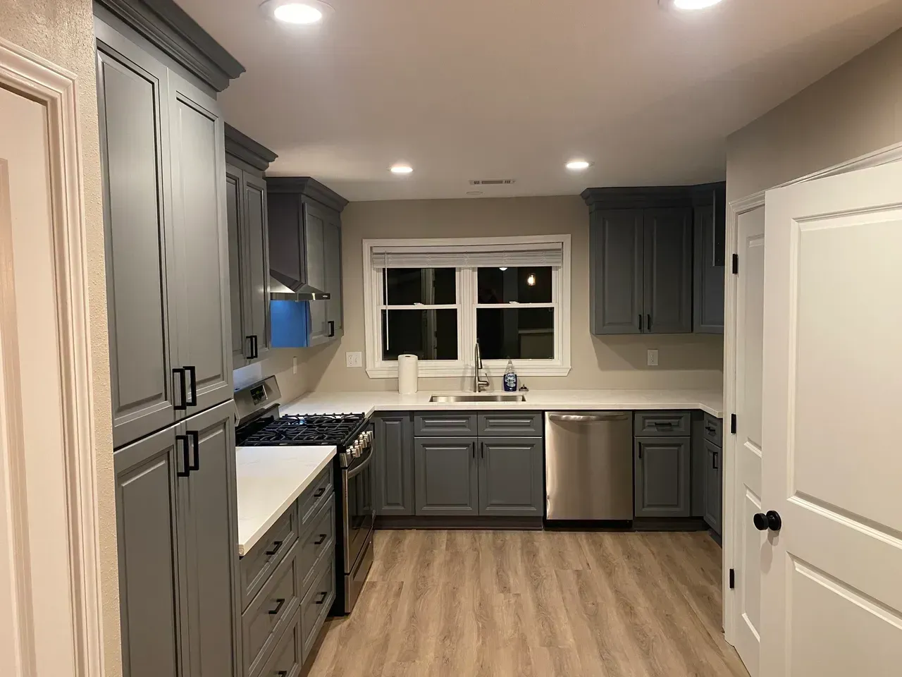 Gray kitchen cabinets with white countertops, stainless steel appliances, and wood-look flooring.