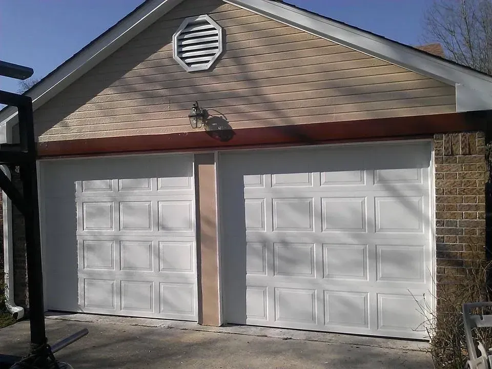 Two white garage doors with brown trim, brick and shingle siding.