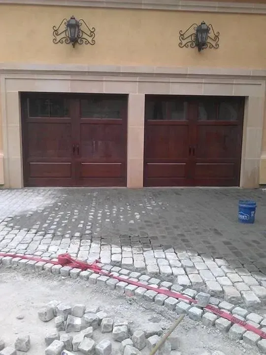 Two dark wood garage doors under a tan building facade, cobblestone driveway under construction.