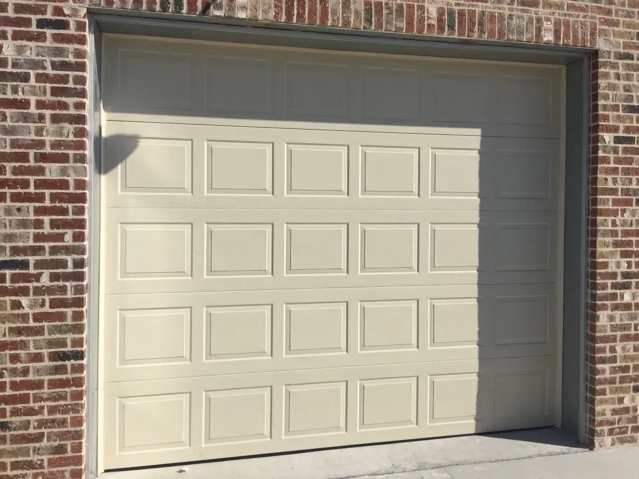 Beige garage door with raised square panels in brick building.