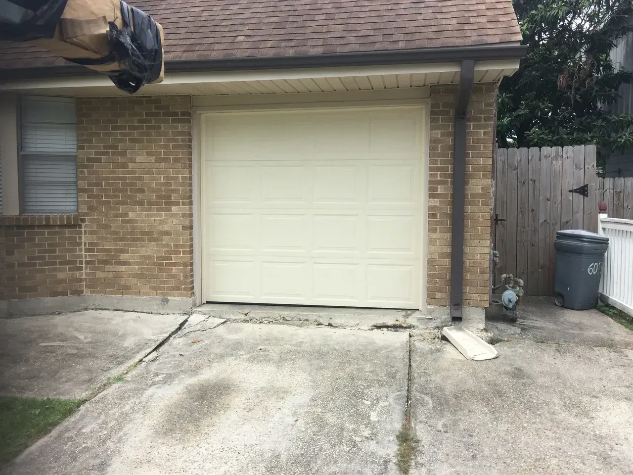 Garage door in a tan brick building; cracked concrete driveway in front.