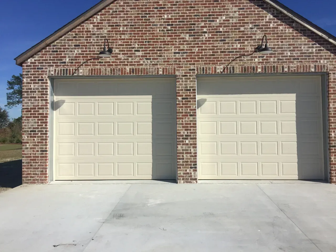 Two beige garage doors in a brick building with concrete driveway.