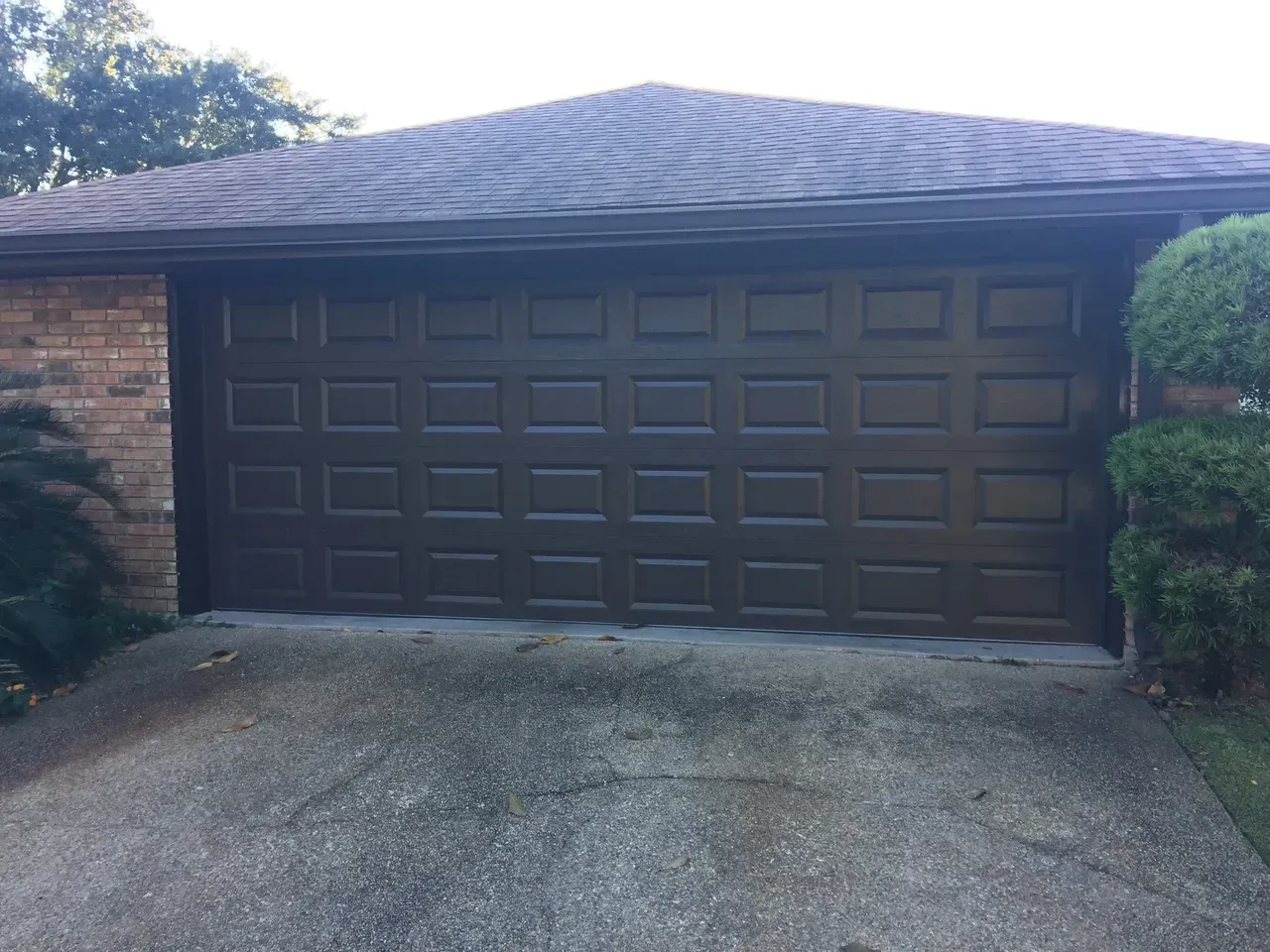 Brown garage door on a house with a concrete driveway and brick siding.