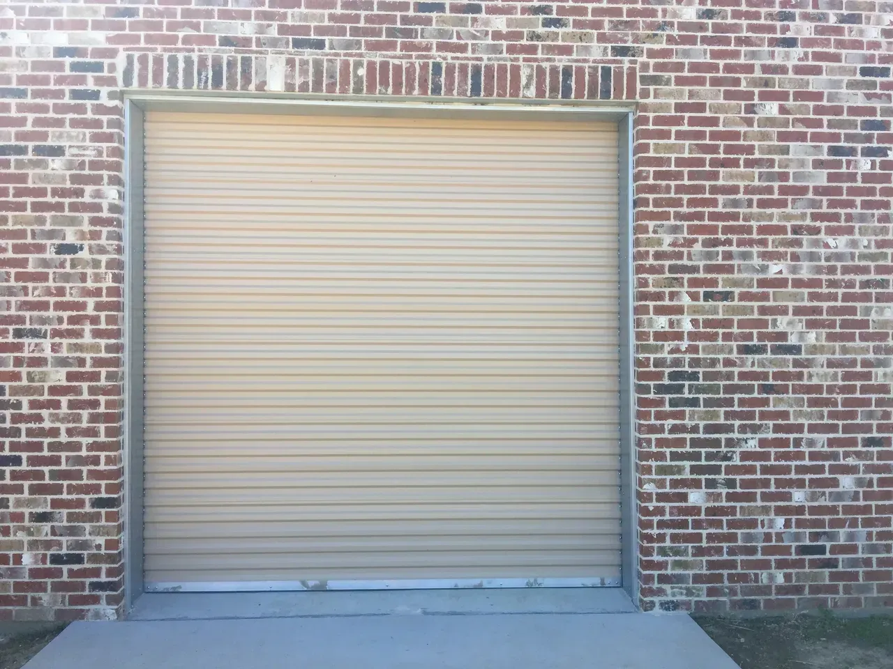 Tan roll-up garage door in a brick building.