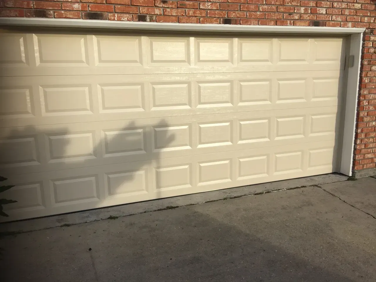 Beige paneled garage door, set in brick building, with shadow across front.