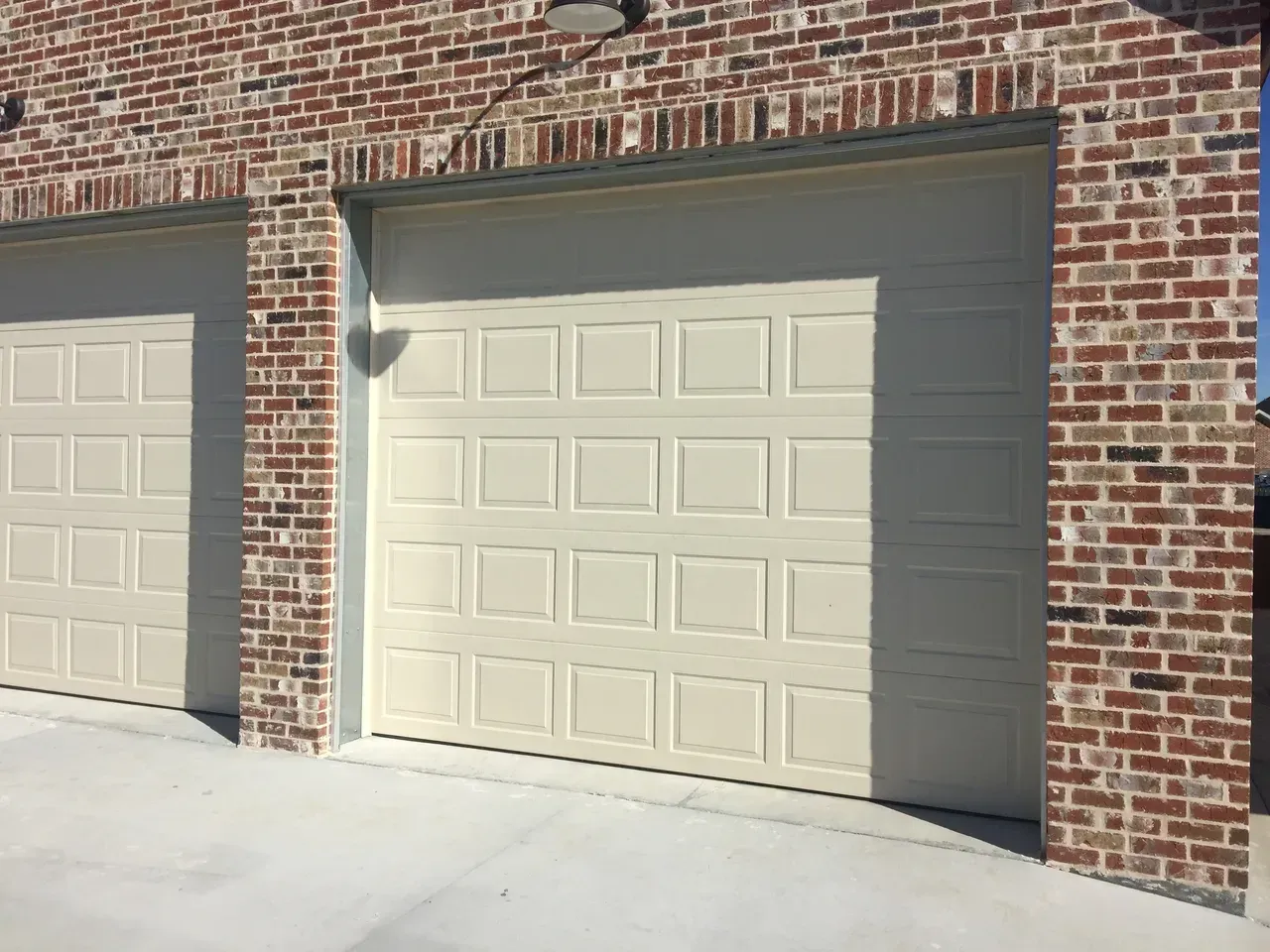 Two beige panel garage doors set in a red brick building.