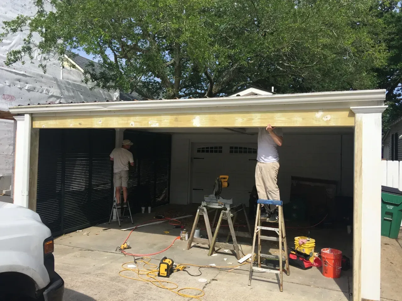 Two people work on a garage roof with scaffolding; tools and materials scattered.