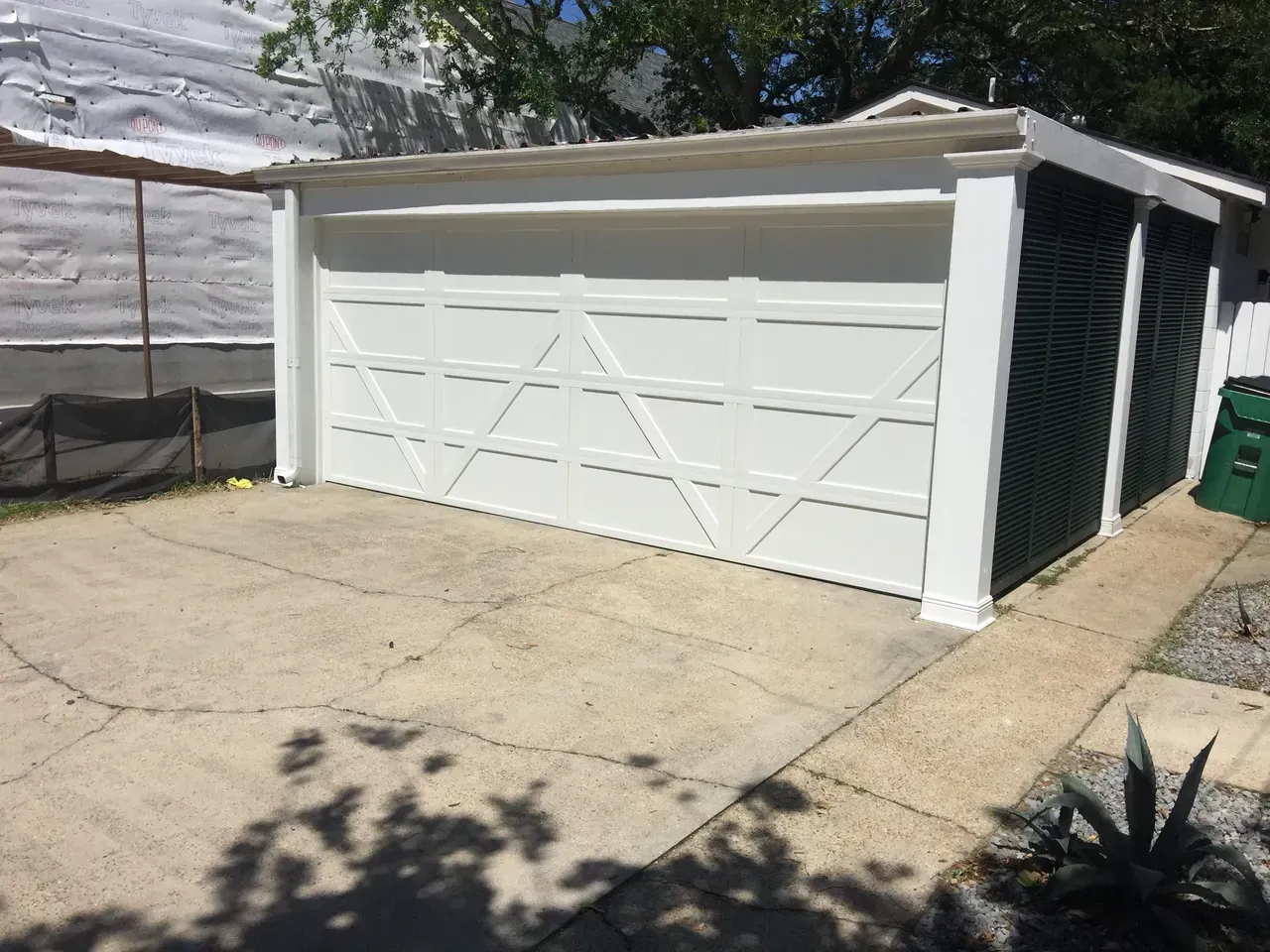 White garage with a concrete driveway and walkway. Green trash can on the side.