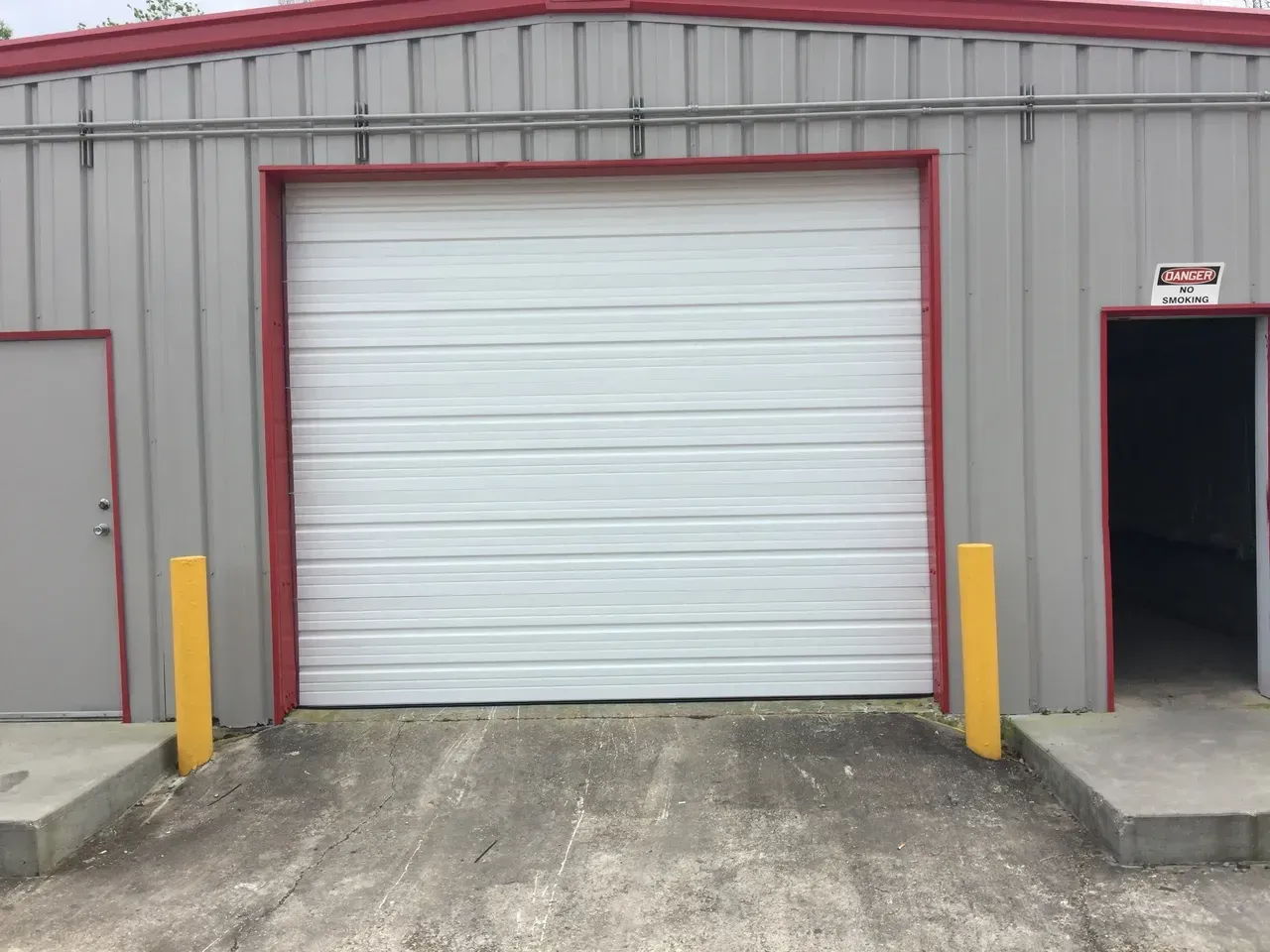 Warehouse with a closed white garage door, red trim, and yellow safety posts.