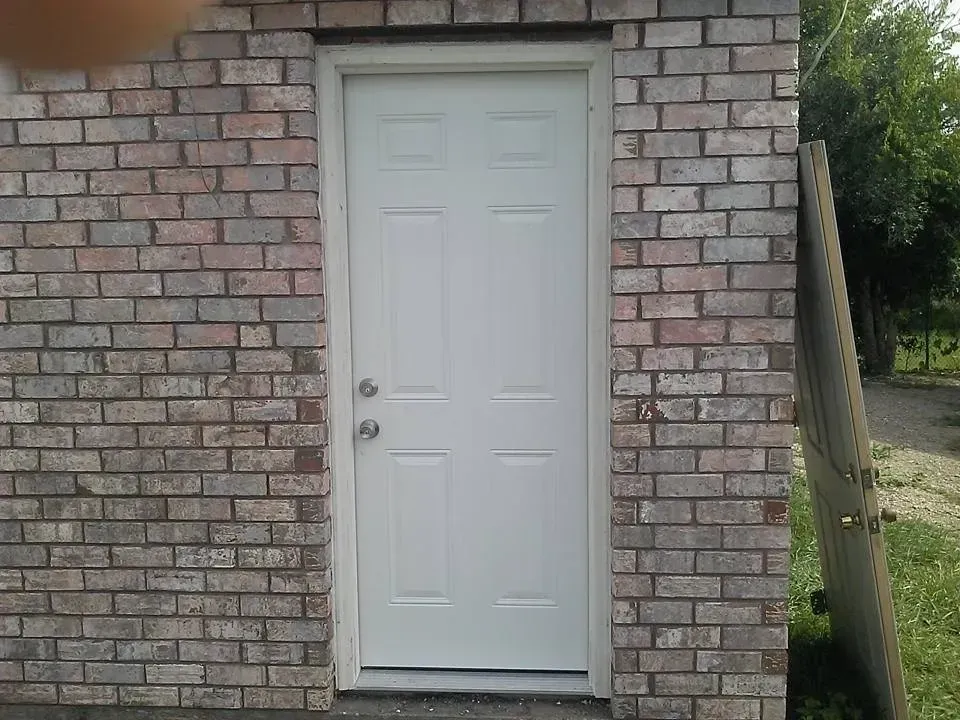 White door set in a brick wall. A weathered wooden fence is adjacent.