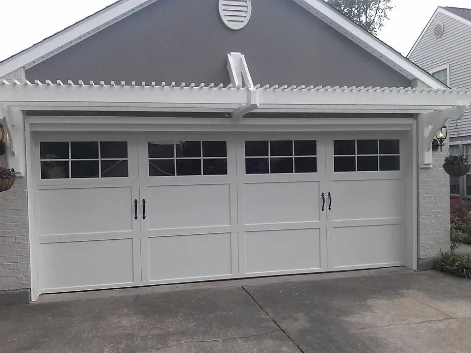 White garage door with windows, under a grey roof and white pergola.