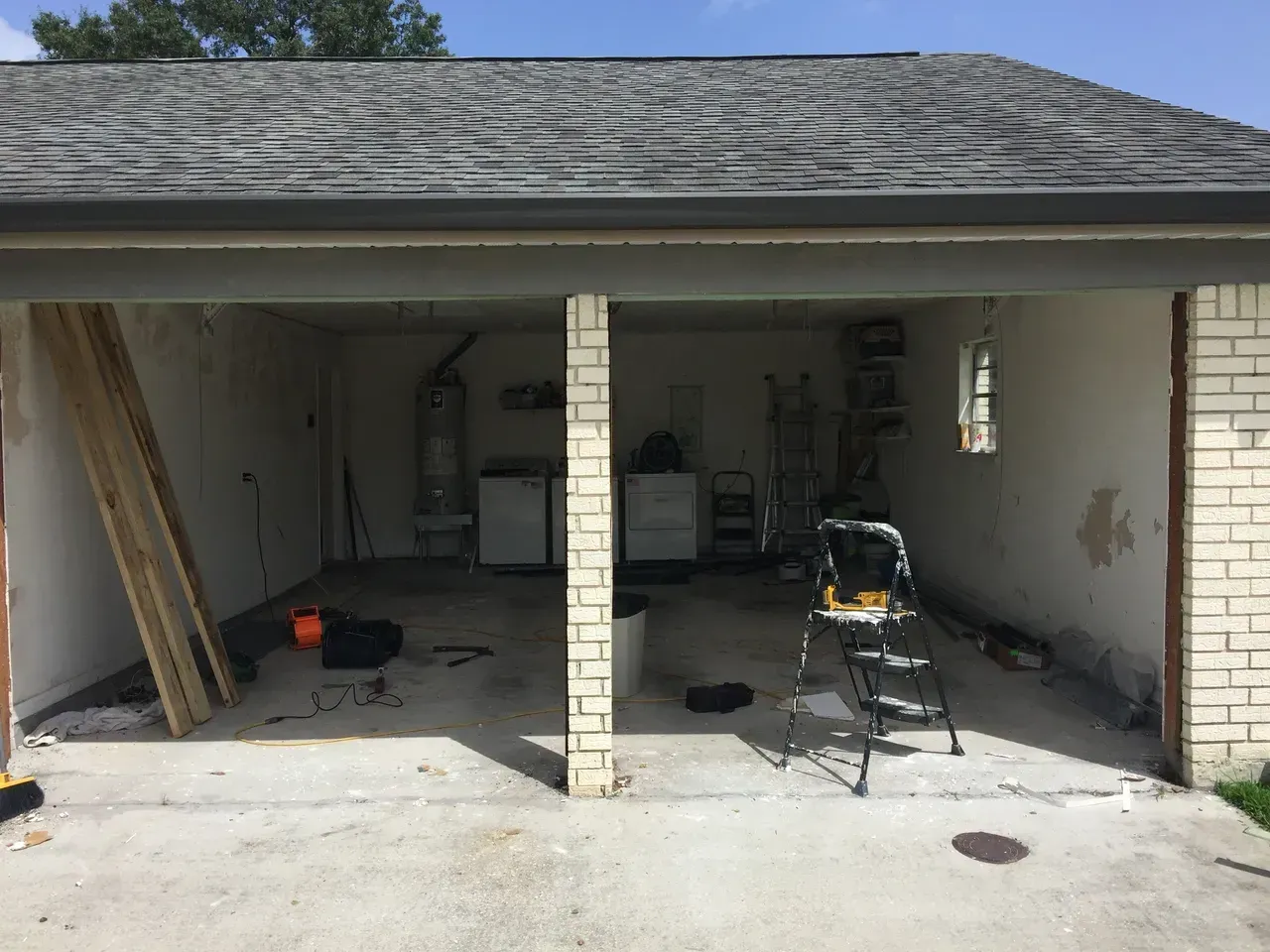Open garage interior with exposed walls, tools, and materials; brick columns divide the space.