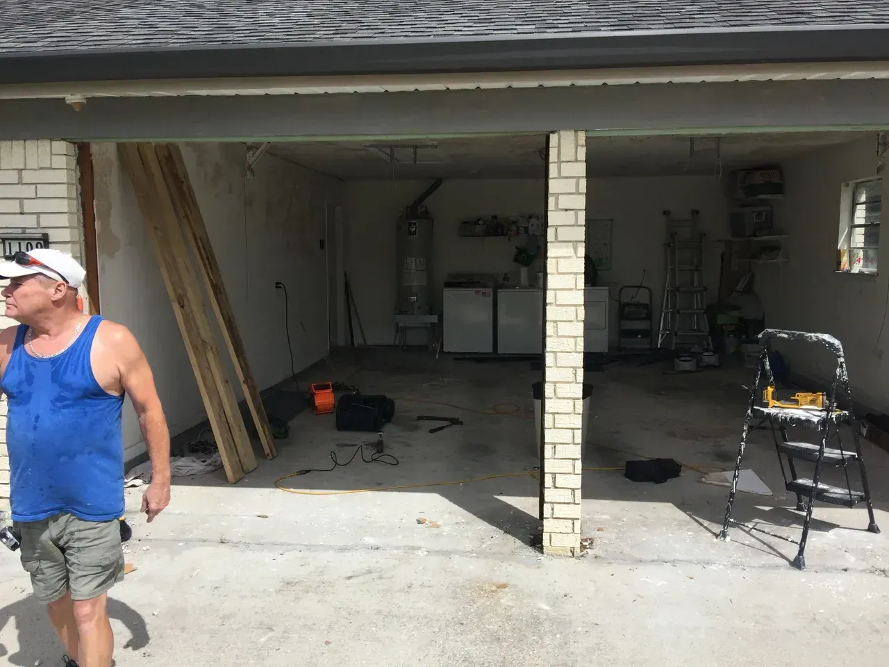 Man in blue tank top looks at partially constructed garage.
