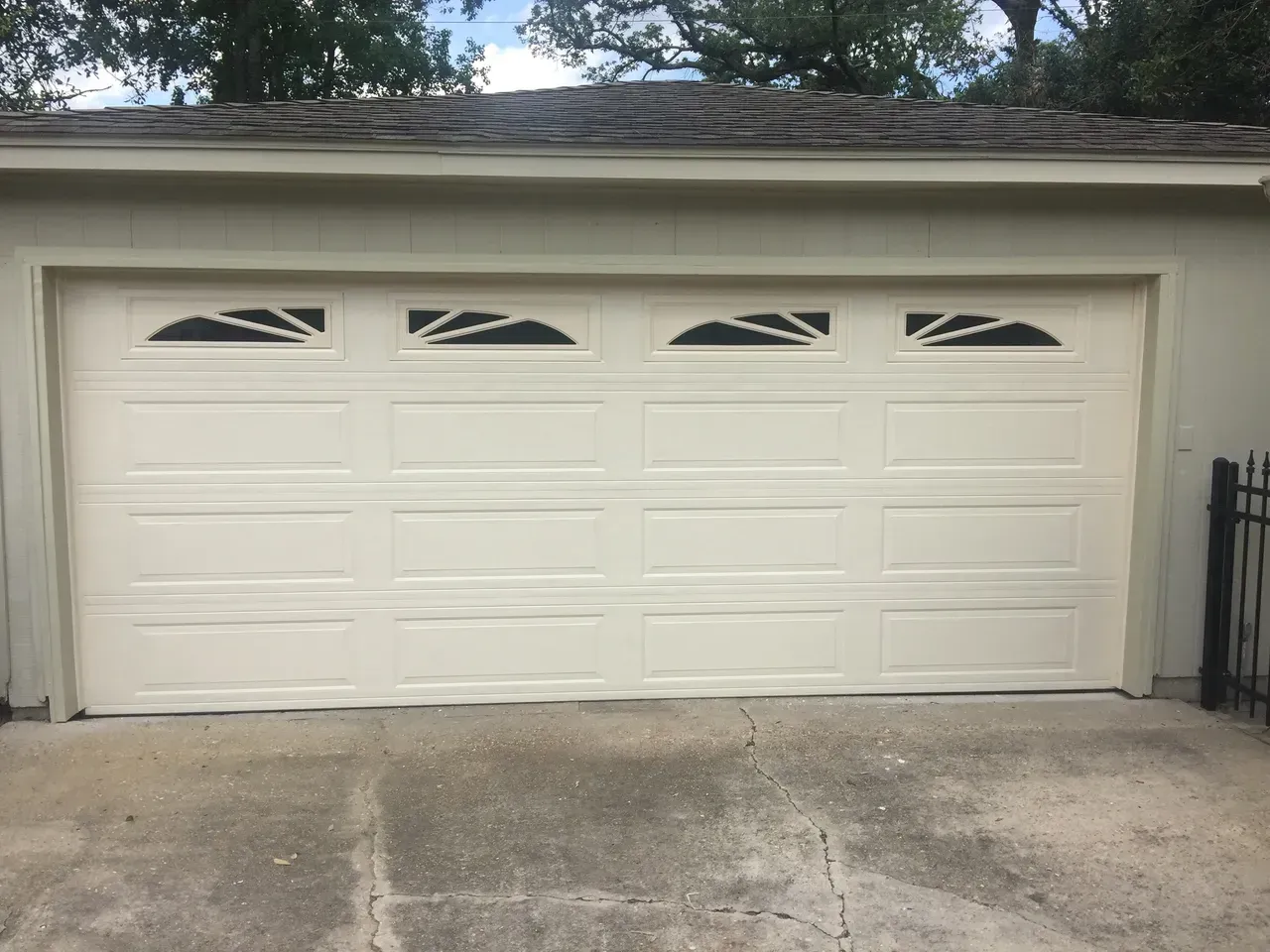 Cream-colored garage door with four windows and decorative black accents; concrete driveway.