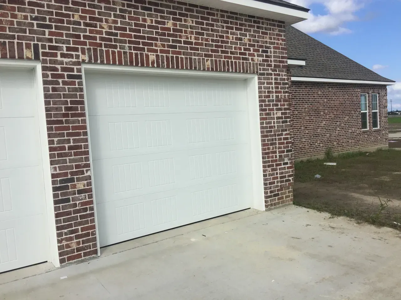 White garage doors on a brick house with concrete driveway.