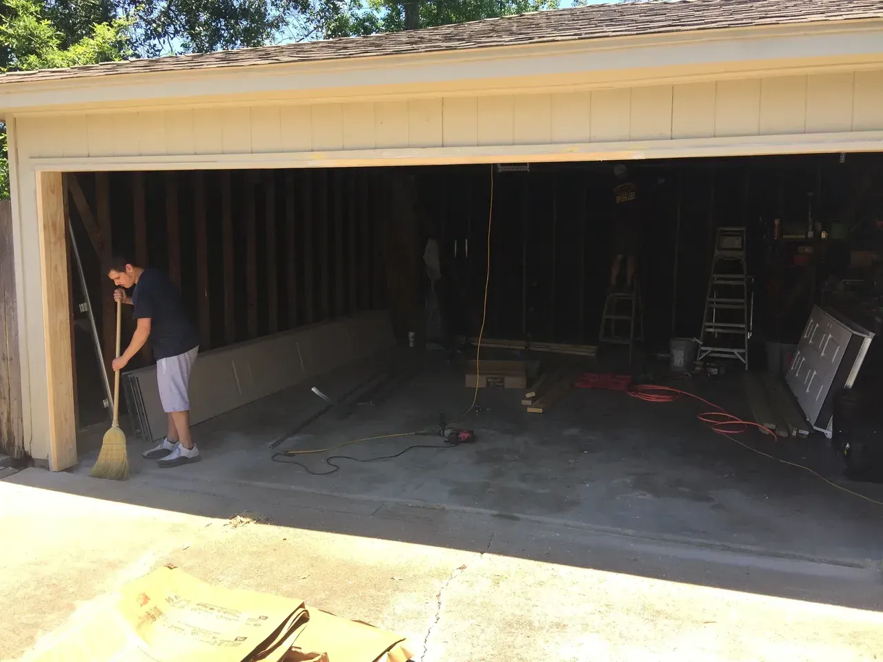 Person sweeping a garage under renovation; wood framing visible.