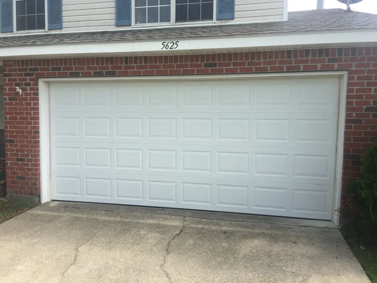 White garage door on a brick building with cracked concrete driveway.