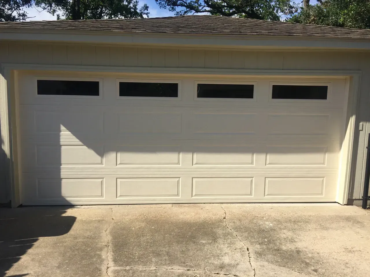 Cream-colored garage door with four rectangular windows. Concrete driveway. Daytime.