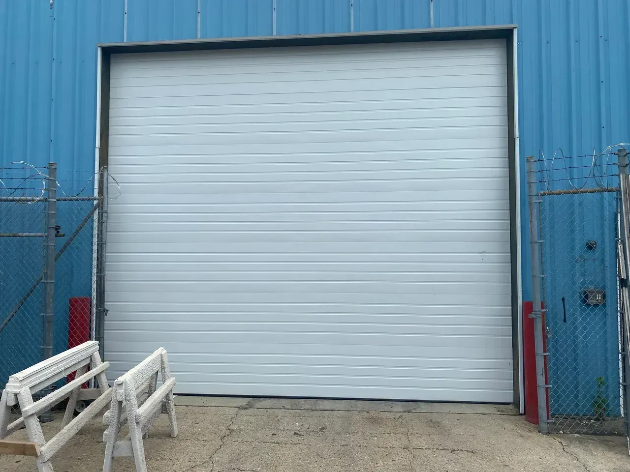 White closed overhead door on a blue building with two saw horses in front.