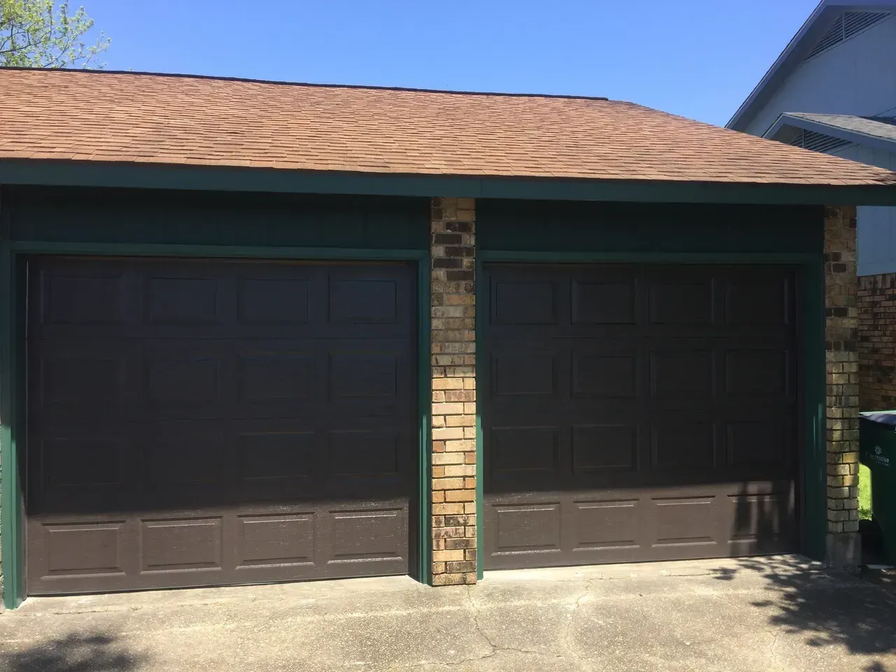 Brown double garage doors with brick and green trim, under a brown roof.