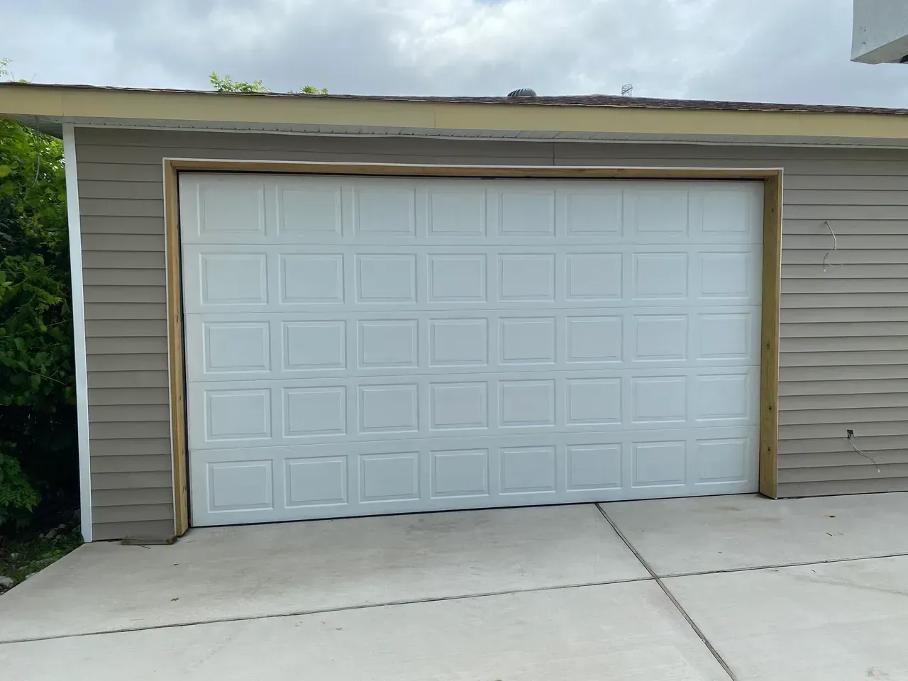 White garage door on a tan building with concrete driveway and a cloudy sky overhead.
