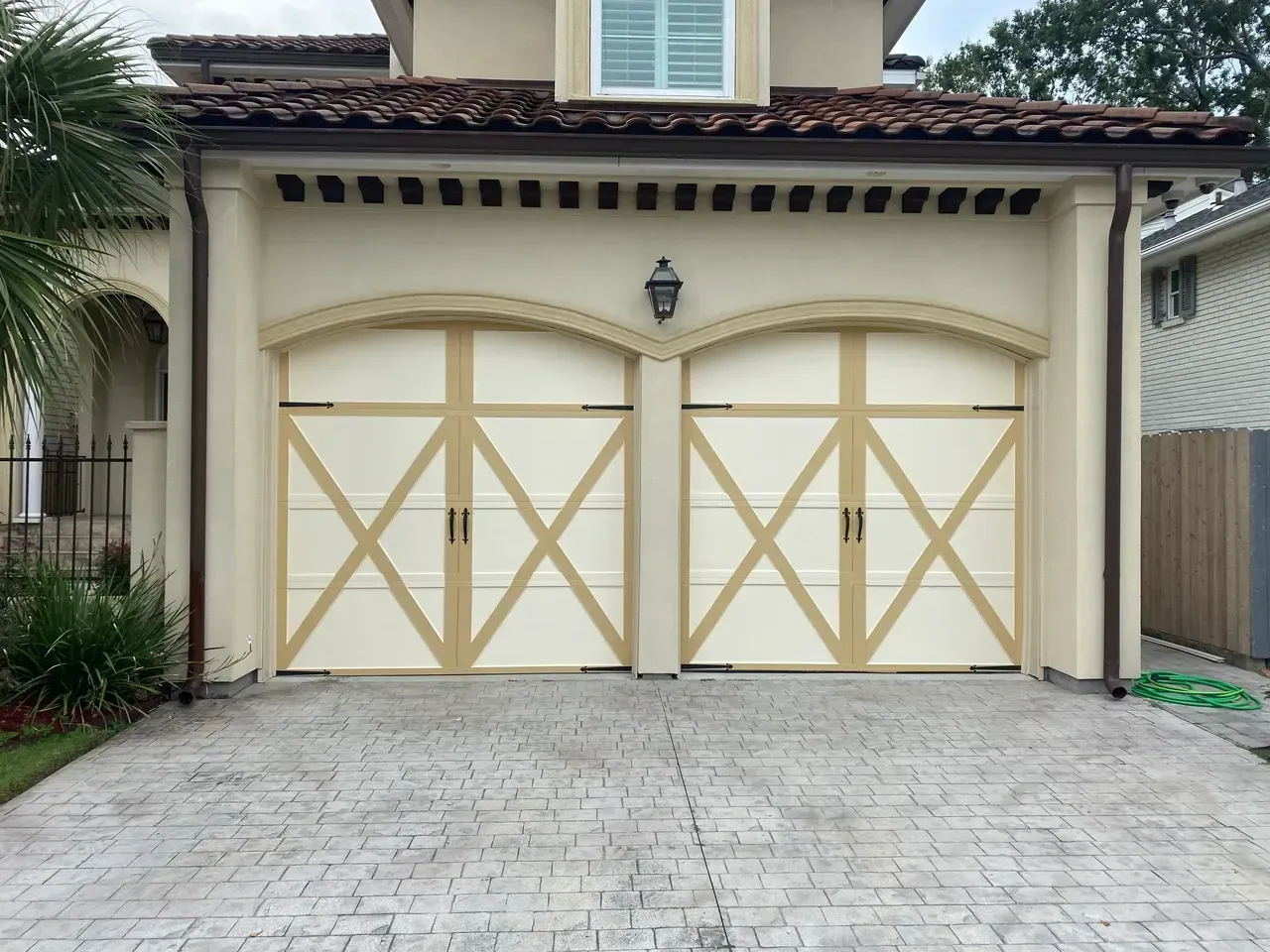 Two cream-colored garage doors with tan cross-bracing and arched tops on a beige house.