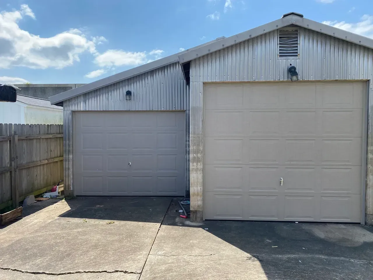 Two gray garage doors in front of a corrugated metal building, on a concrete driveway.