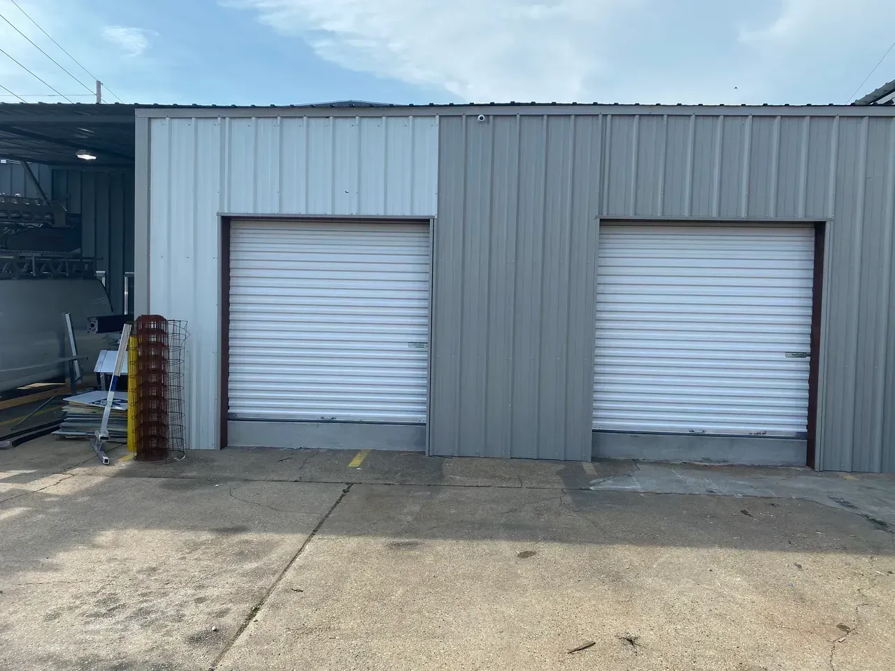 Two gray metal warehouse bays with white roll-up doors on a concrete lot.