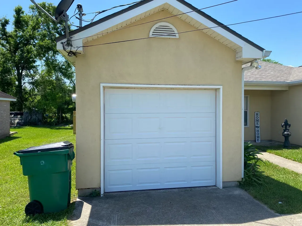 Tan garage with white door, green trash can, and sidewalk.