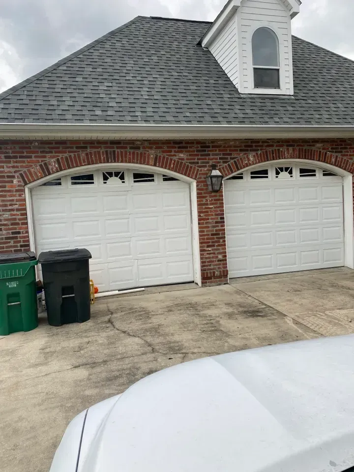 Two white garage doors on a brick house with a dark gray roof. Trash cans in the front.