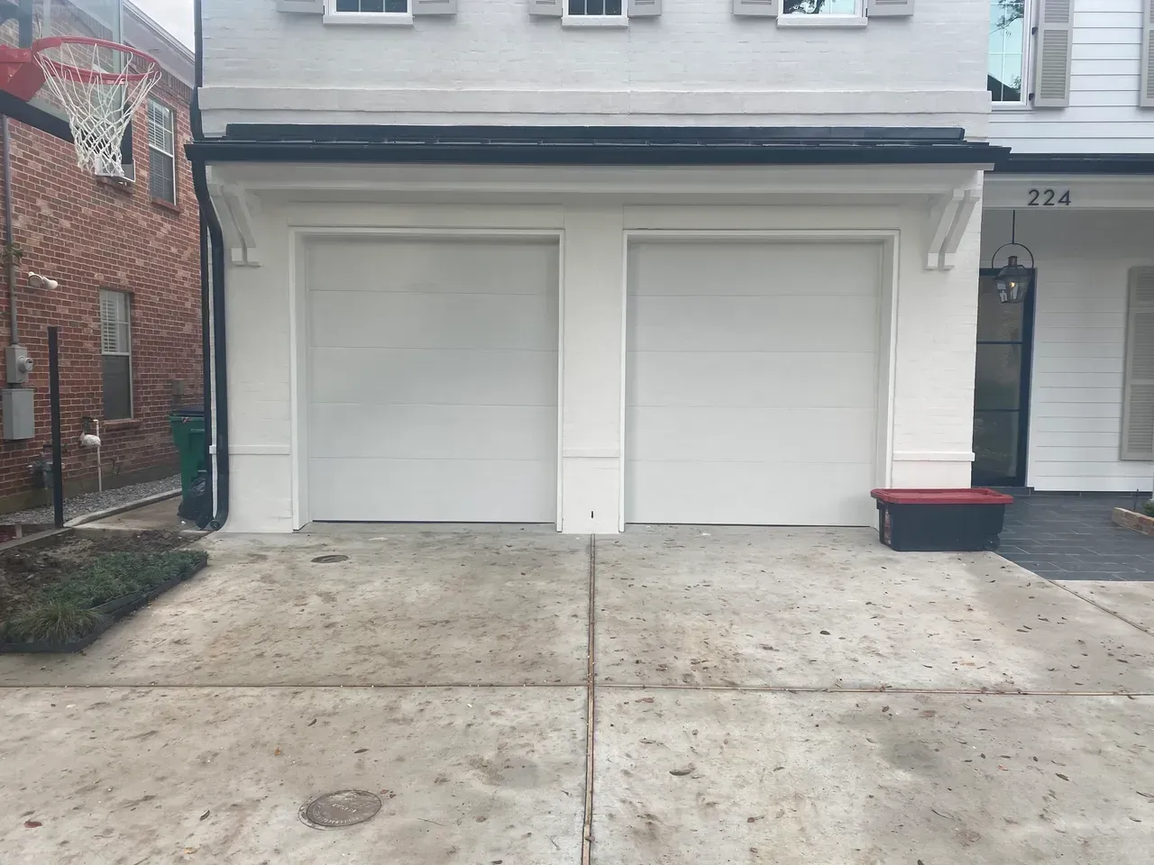 Two white garage doors with white trim on a concrete driveway.