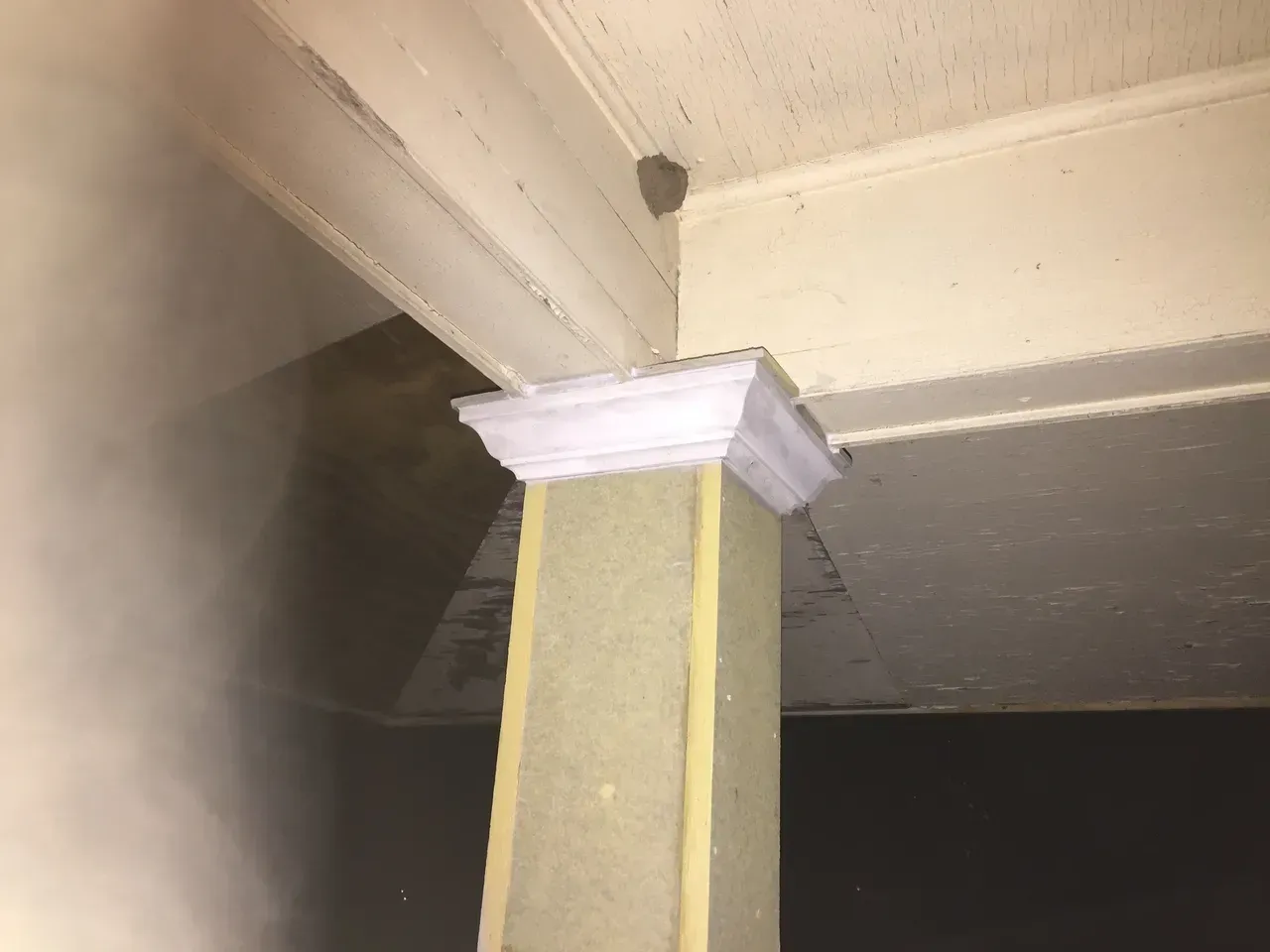 Cream-colored porch corner with column, crown molding, and possible wasp nest in the upper corner.
