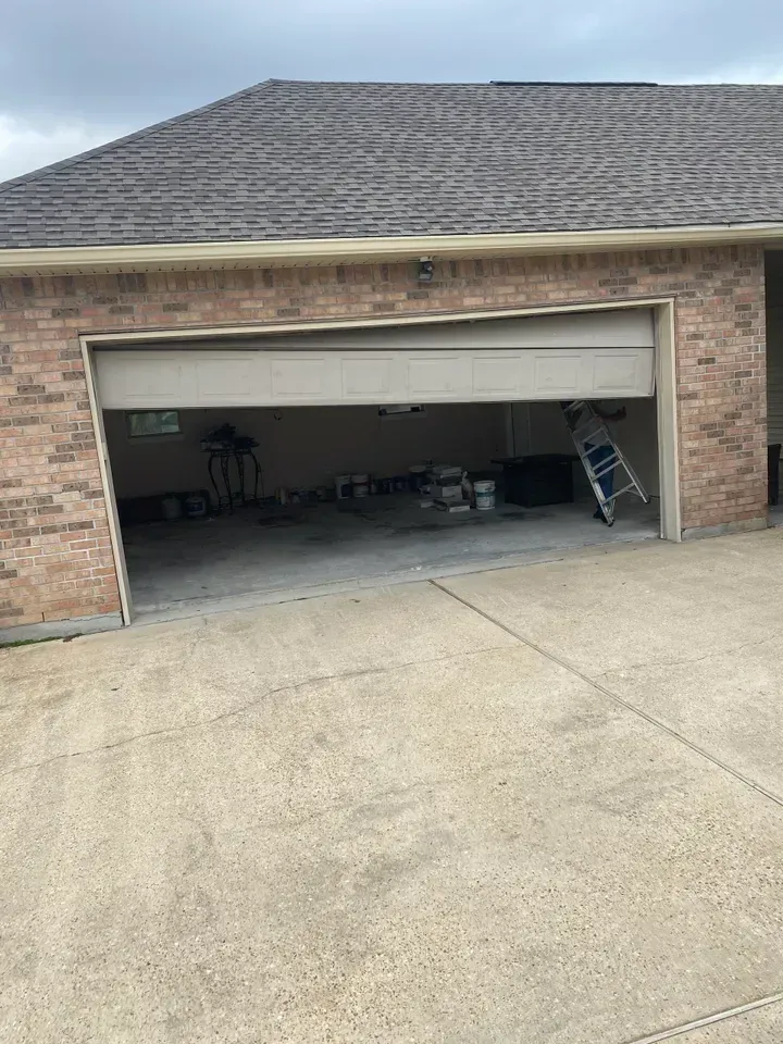 Garage with partially open door, brick exterior, concrete driveway. Ladder and various items inside.
