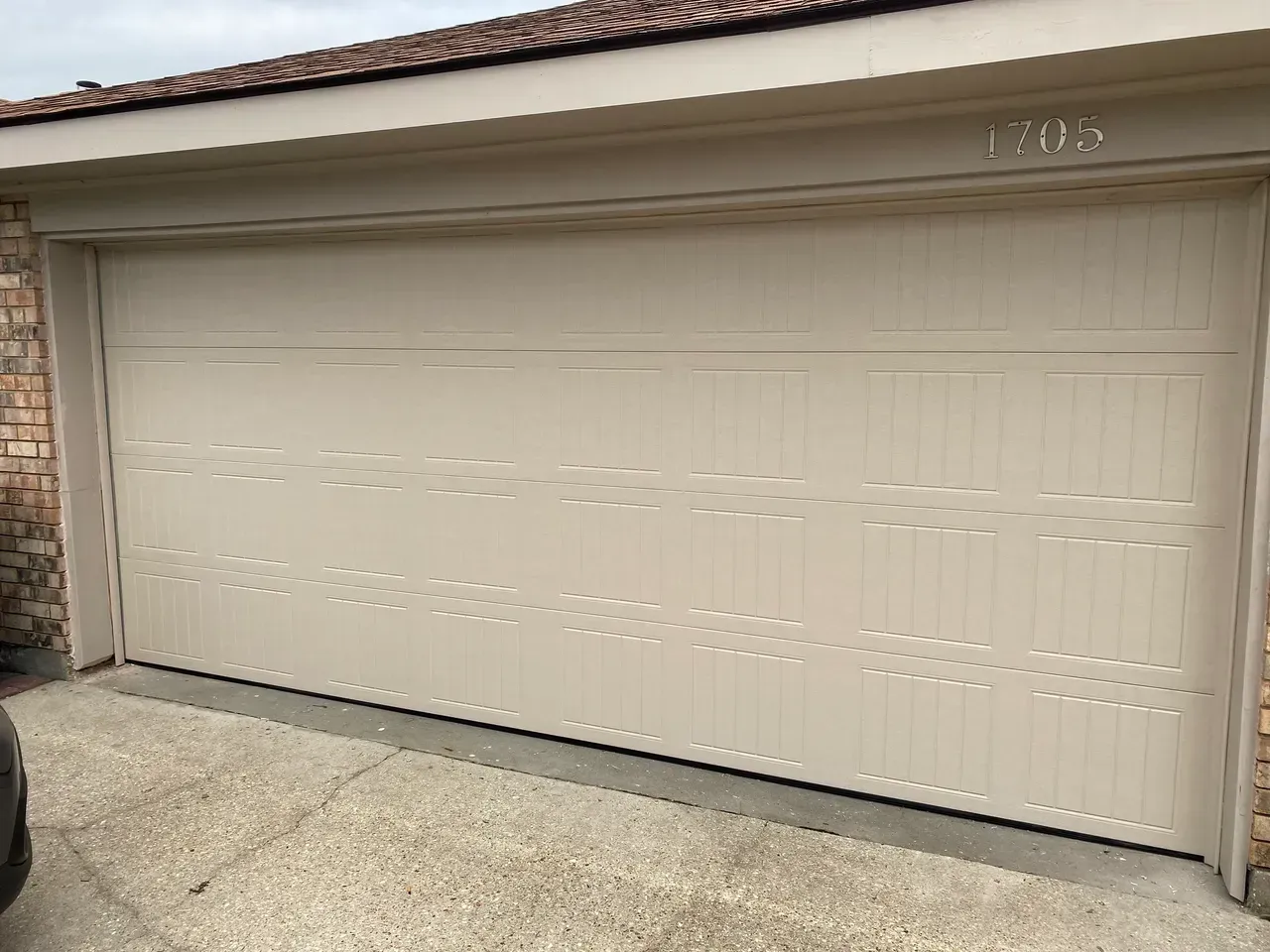 Tan garage door with brick siding, number 1705 above. Concrete driveway.
